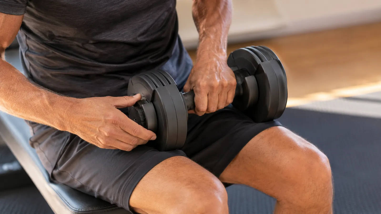 Hands adjusting the weight mechanism on a dumbbell during a home workout, gym mat underneath