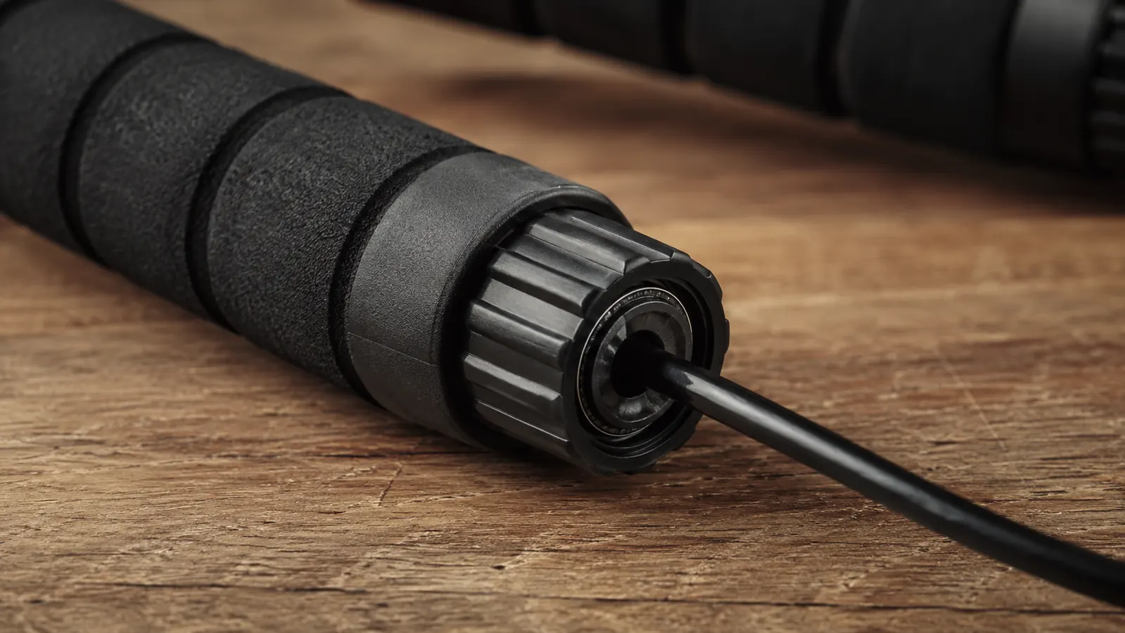 Close up of a jump rope handle showing the foam grip, the screw-cap adjustment mechanism, and the PVC cable exiting the handle