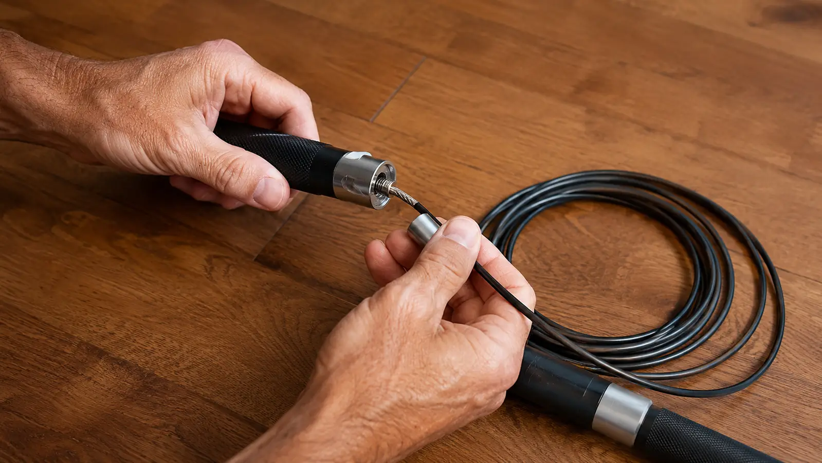 Hands adjusting the length of a jump rope on a hardwood floor with the cable coiled beside it